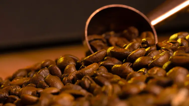 Granos de café saliendo de una cuchara de cobre